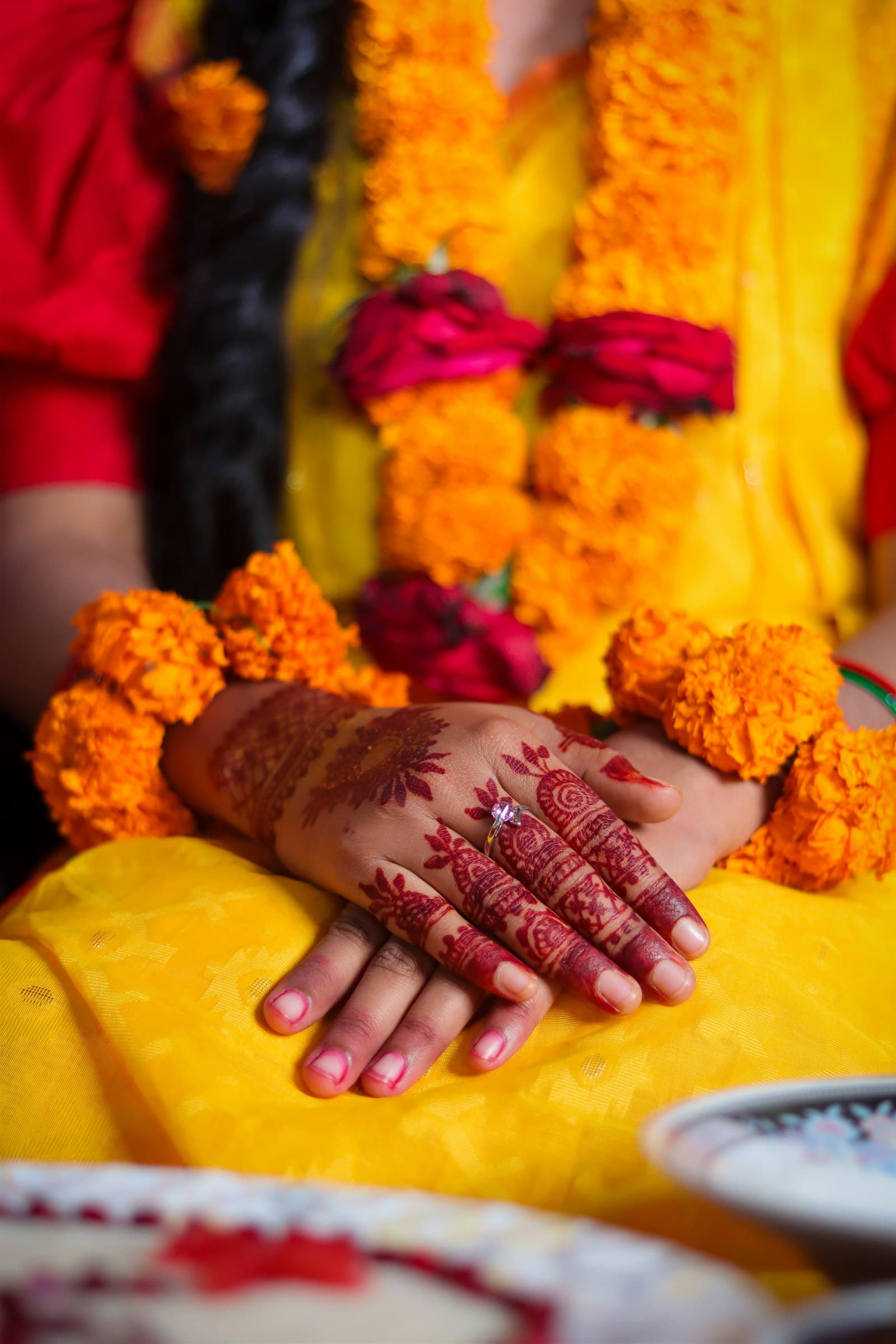 A bride’s hennaed hands resting on marigold garlands