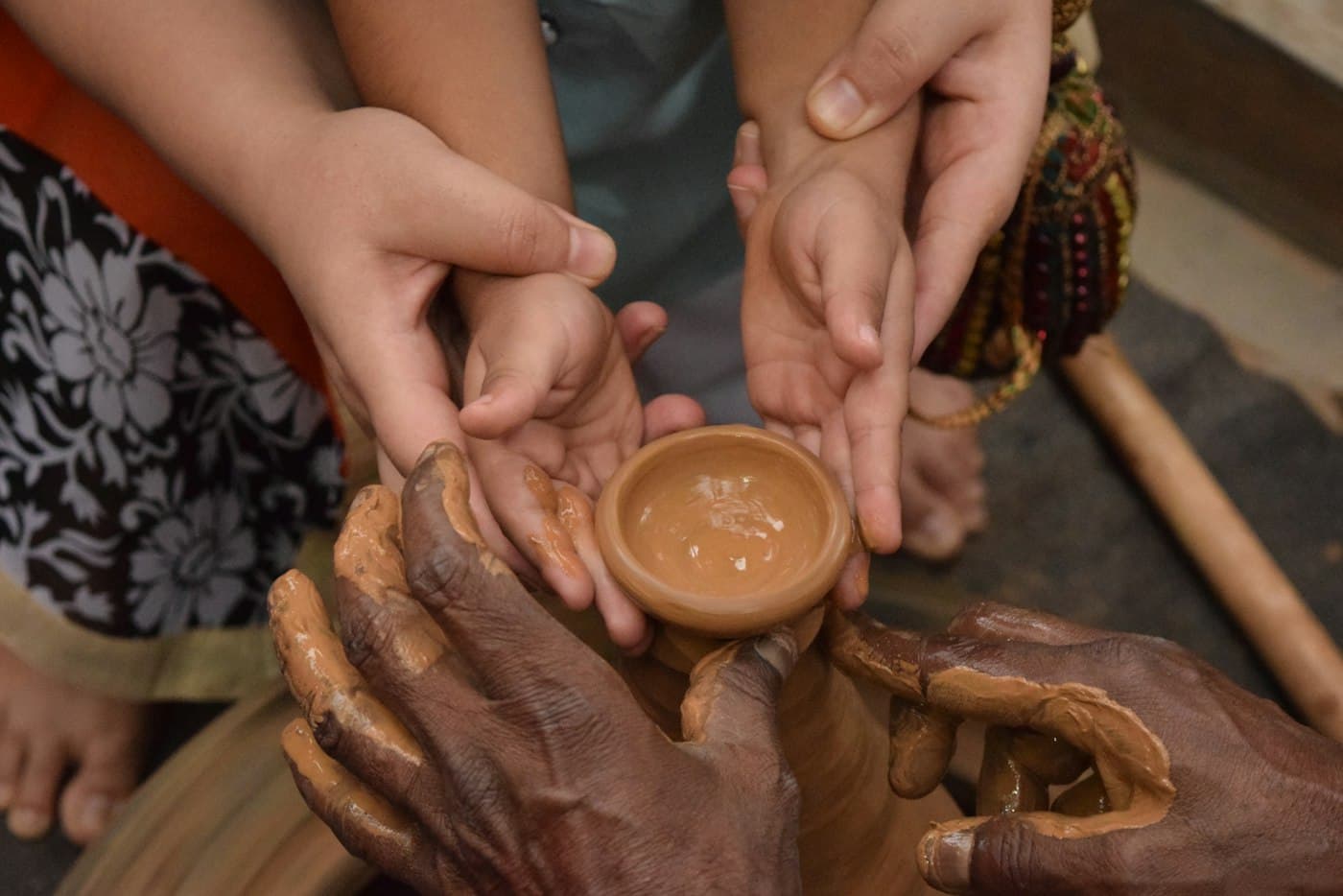 Many hands holding a small clay cup together