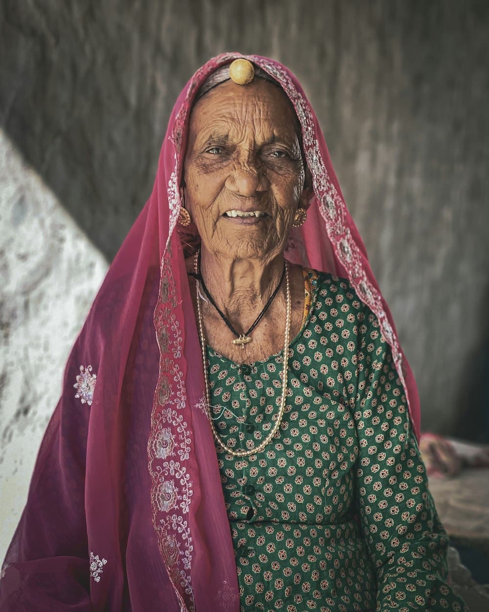 An elderly woman in a red odhni, smiling