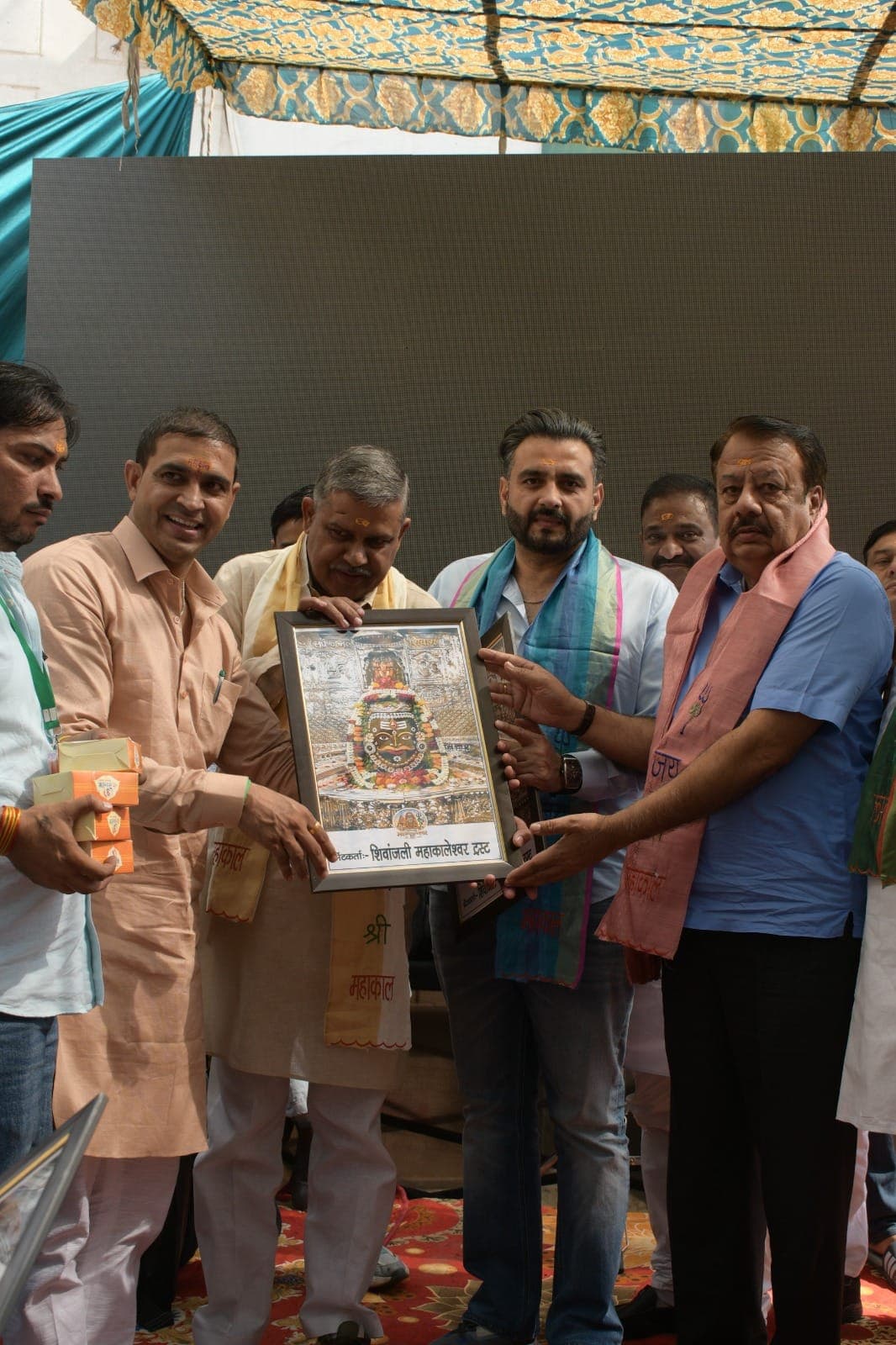 मंच पर देवेंद्र कादयान का महाकाल के फ्रेम किए चित्र के साथ स्वागत