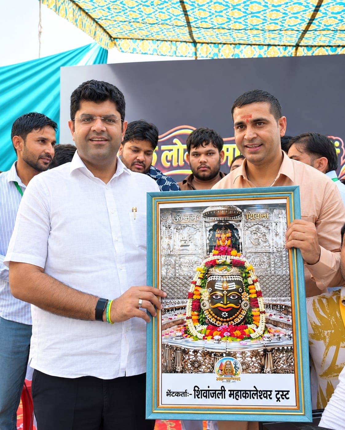 मुख्य अतिथि दुष्यंत चौटाला और ट्रस्ट के संस्थापक रविंदर सांगवान ट्रस्ट की ओर से भेंट किया महाकालेश्वर का फ्रेम किया चित्र थामे हुए