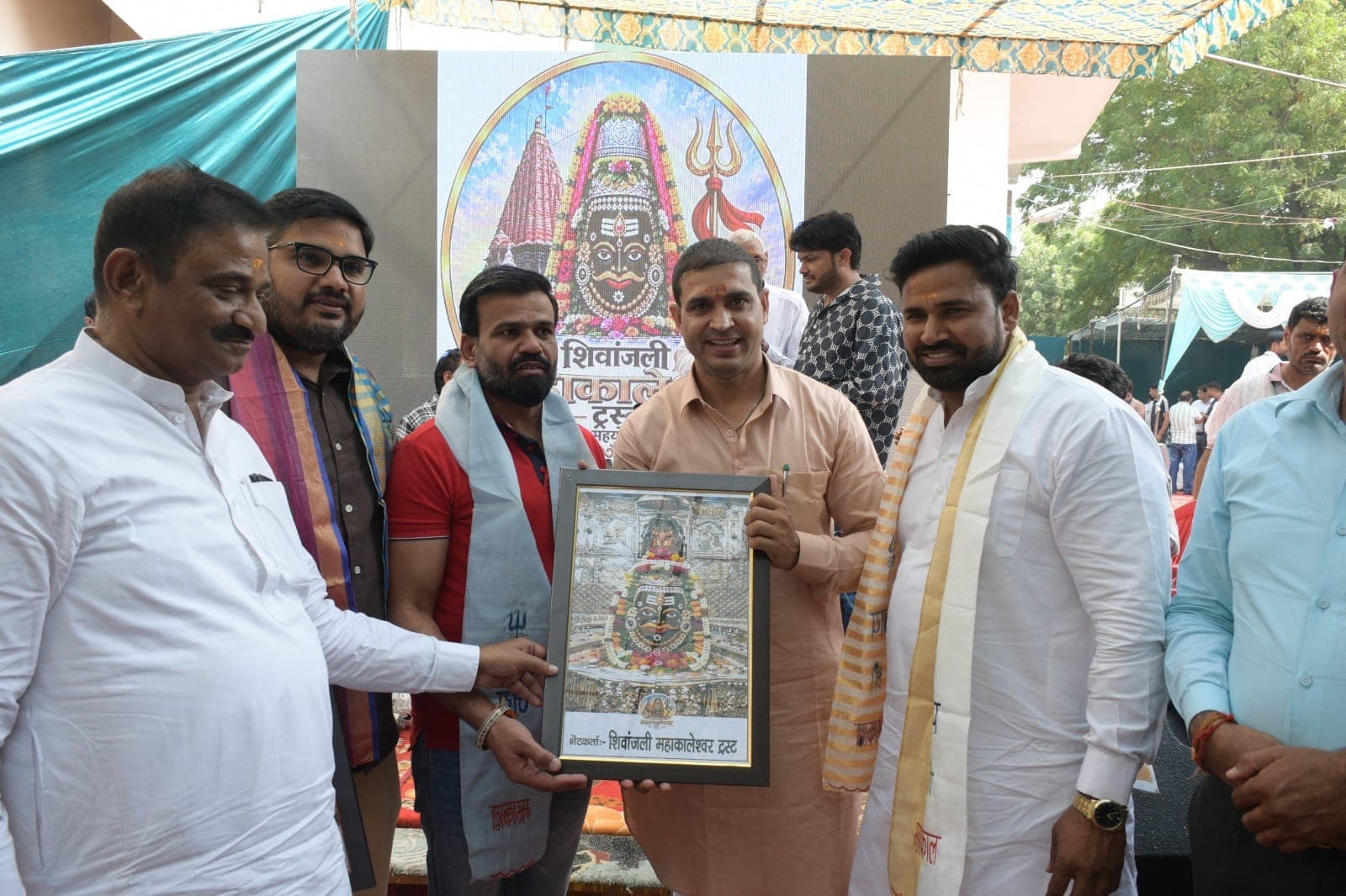 ट्रस्ट के महाकाल बैकड्रॉप के सामने अतिथियों और फ्रेम किए चित्र के साथ रविंदर सांगवान